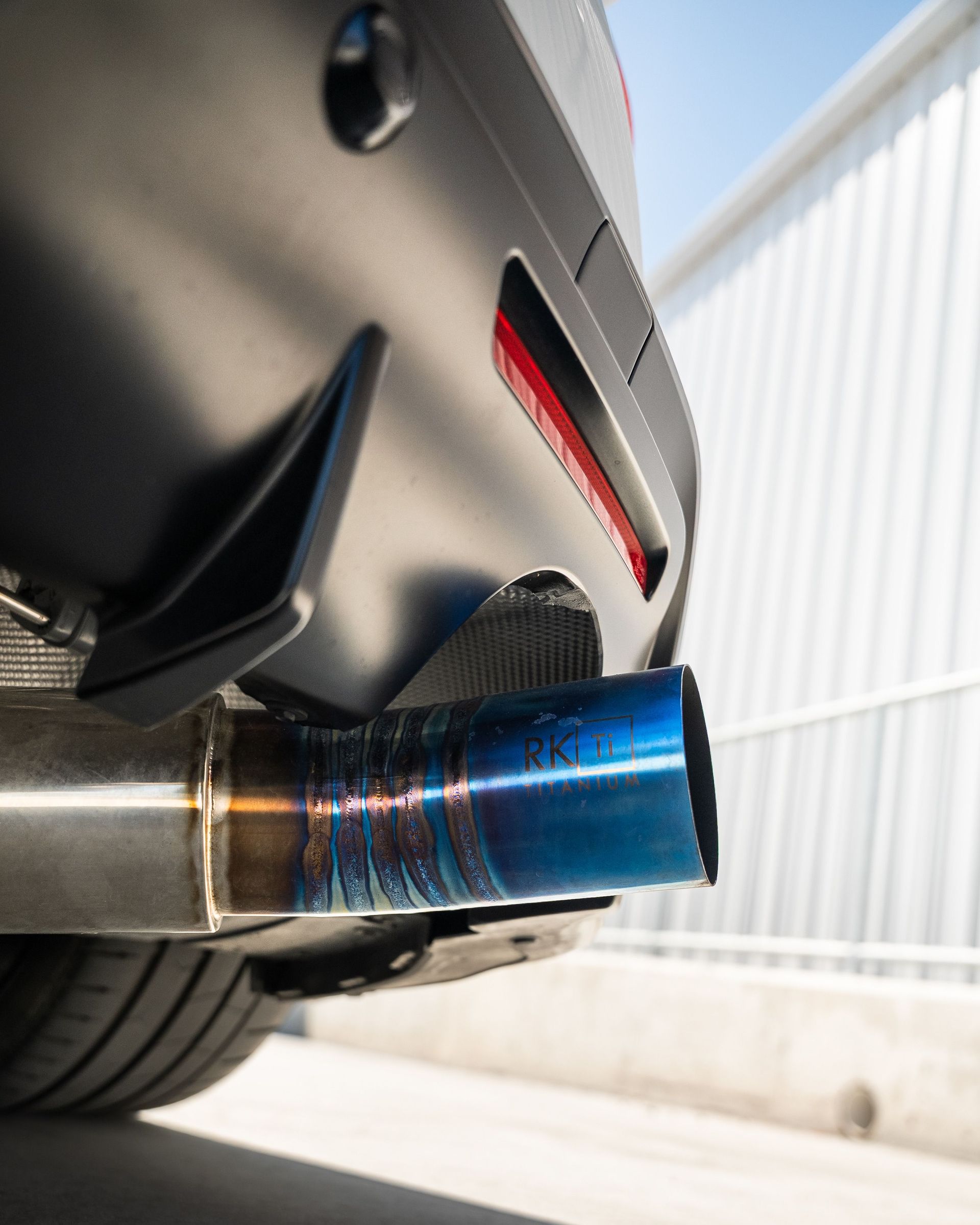 Detailed view of a sports car's exhaust pipe in bright sunlight, emphasizing modern automotive design.